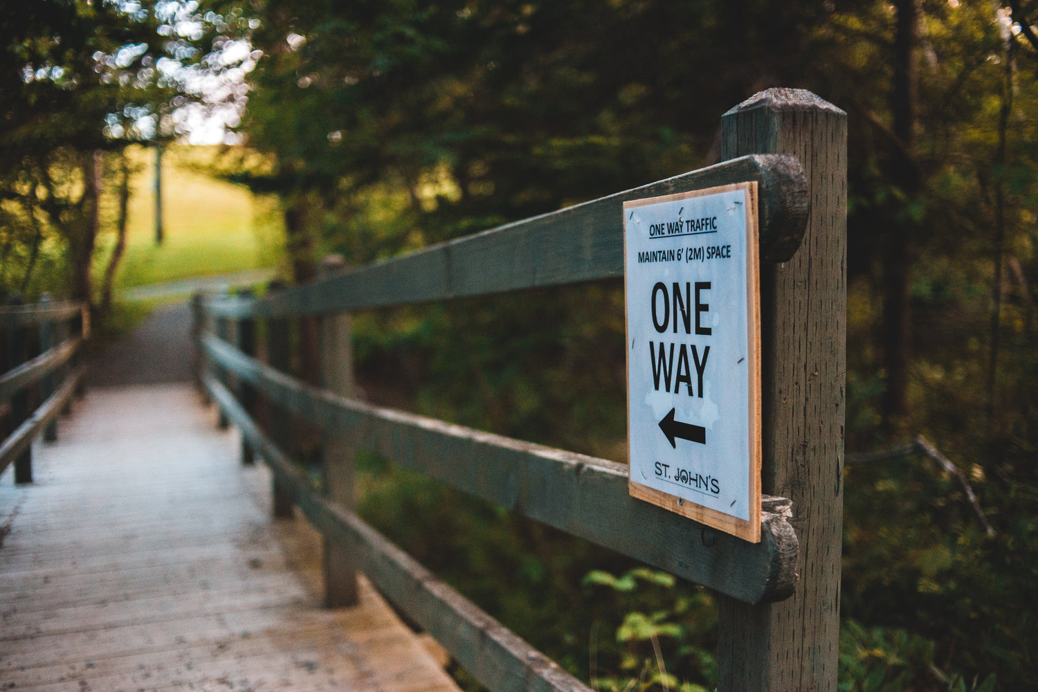 Wooden bridge surrounded by trees and a sign saying one way