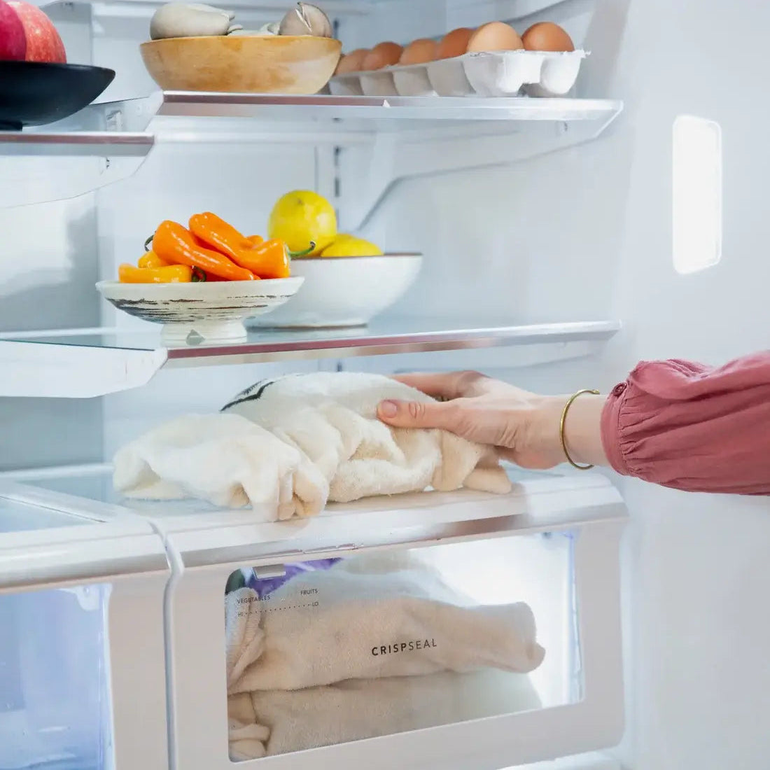 Open refrigerator with various food items inside, including a hand reaching in.