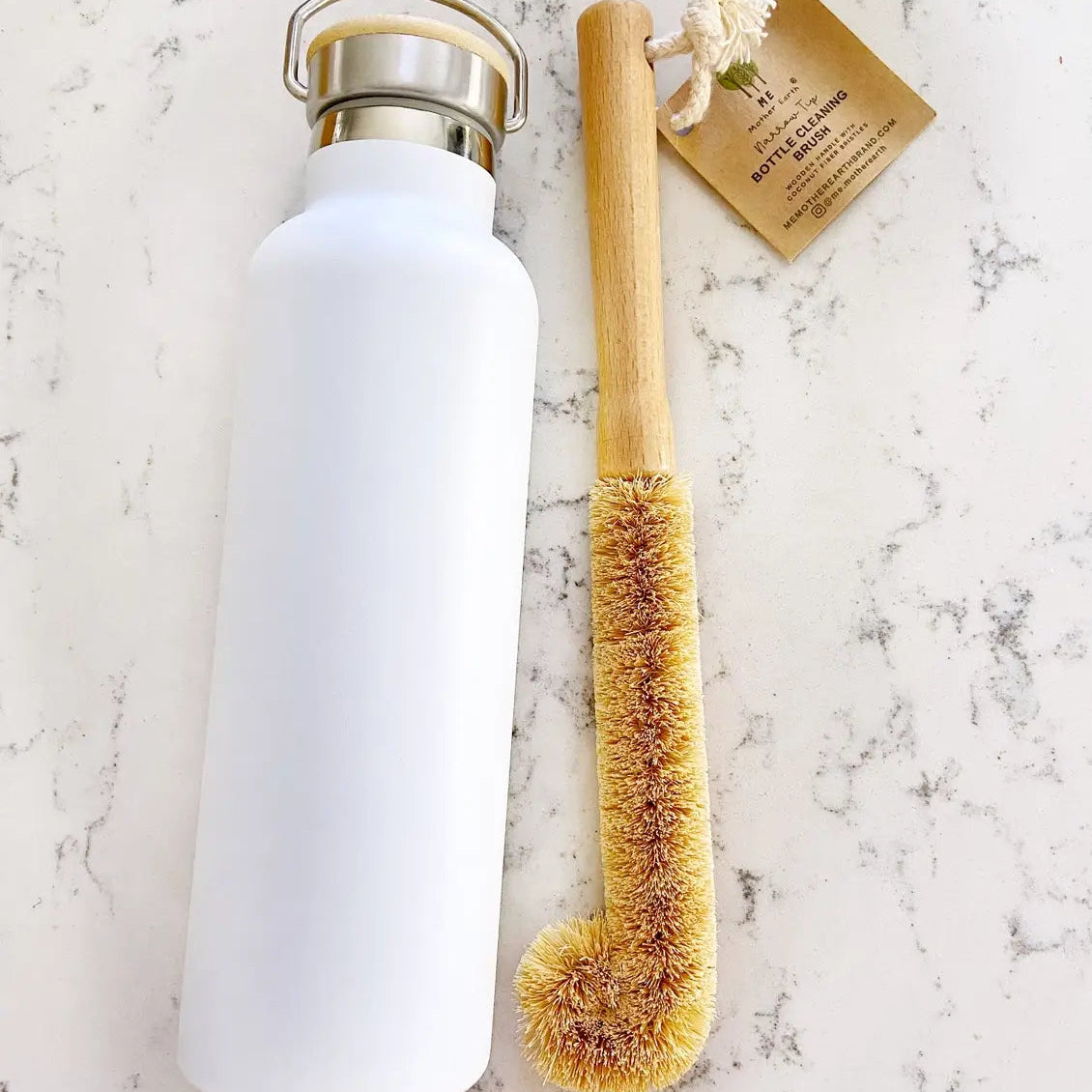 White water bottle with metal cap and natural bristle brush on a marble surface