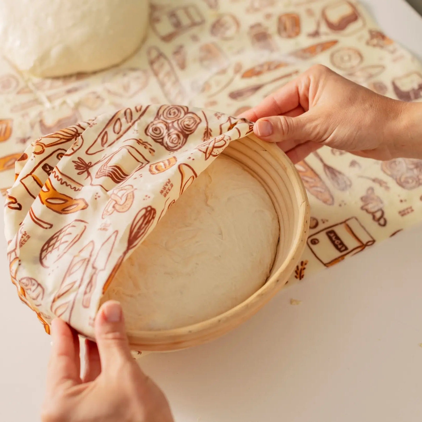 Person using a bee's wrap wax to cover a sourdough in a proofing basket on a countertop