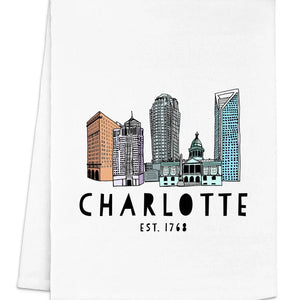 A folded white dish towel with a colorful illustration of a city skyline and the text 'CHARLOTTE EST. 1768' printed on it.