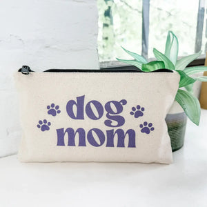 Canvas pouch with 'dog mom' text on a white surface with a plant in the background