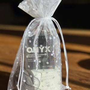 Gift set with a goat milk moisturizer, a bar of soap and a konjac sponge in an organza bag on a wooden surface