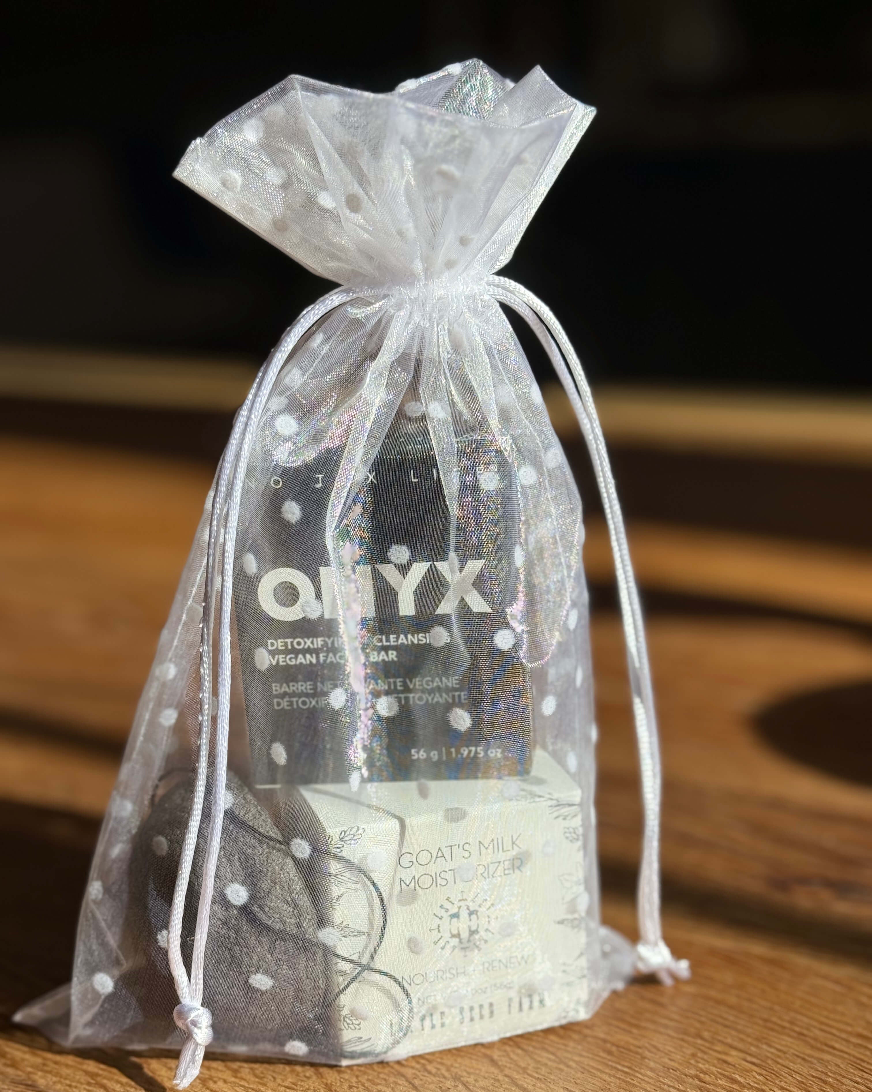 Gift set with a goat milk moisturizer, a bar of soap and a konjac sponge in an organza bag on a wooden surface