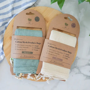 Two organic cotton mesh produce bags on packaging with a wooden board and striped fabric background.