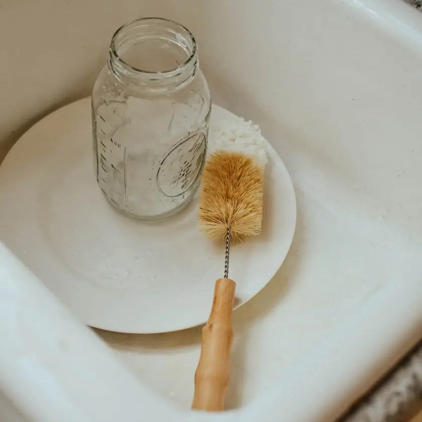 Mason jar and cleaning brush on a white plate in a sink