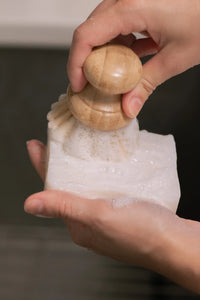 Hand holding a wooden pepper grinder over a container of ground pepper.