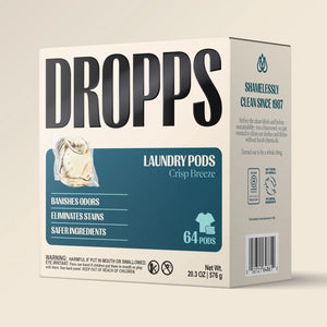 A box of DROPPS Laundry Pods in the Crisp Breeze scent, featuring a white and teal design with product details and a barcode on a light beige background.