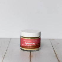 Jar of face mask powder with a red label on a white wooden surface