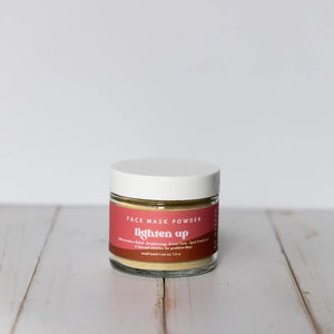 Jar of face mask powder with a red label on a white wooden surface