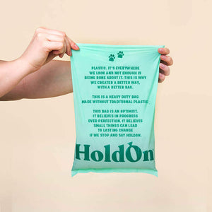 Person holding a compostable dog poop bag with text and 'HoldOn' branding against a beige background