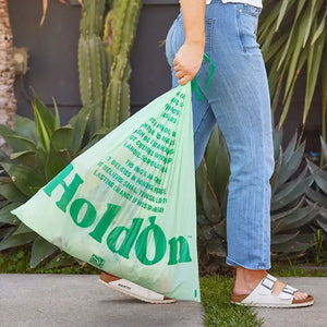 Person holding a green 'HoldOn' bag with plants in the background