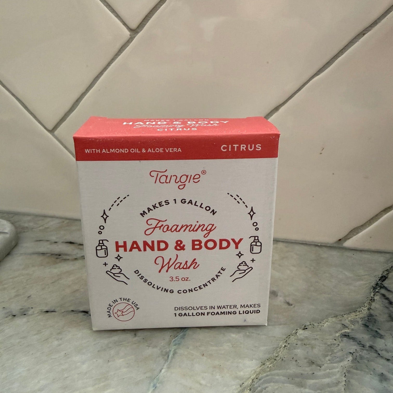 A box of Tangie Hand & Body Foaming Soap in Citrus scent, placed diagonally on a tiled floor.