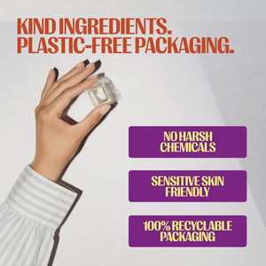 A hand wearing a light blue and white striped shirt holds a small clear plastic packaging cube against a light gray background. Large orange text at the top reads 'KIND INGREDIENTS.