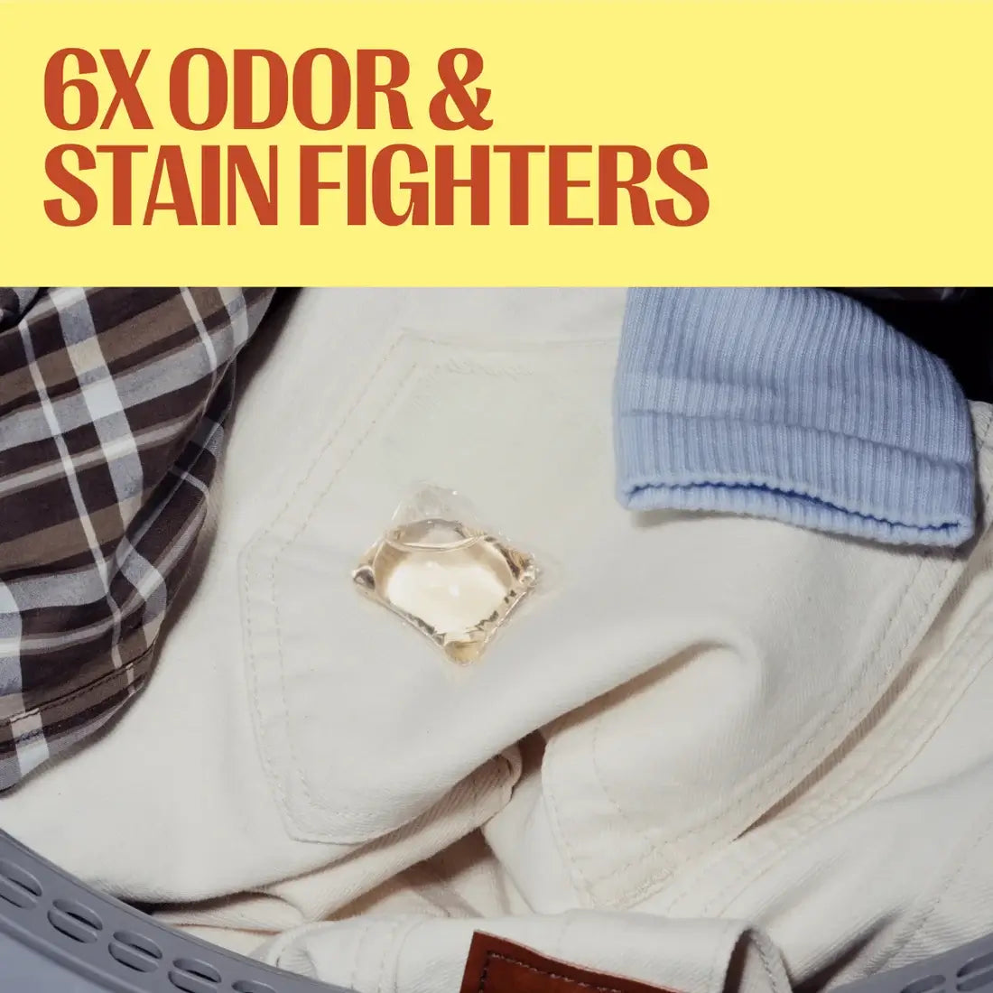 A close-up of folded clothing in a laundry basket with a clear square patch showing a detergent crystal, under a yellow banner with red text reading '6X ODOR & STAIN FIGHTERS'.
