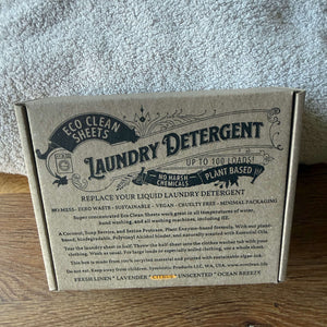 A cardboard box of Eco Clean Sheets Laundry Detergent placed on a wooden surface with a gray textured towel behind it.