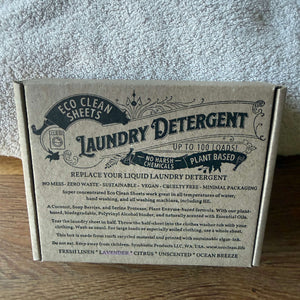A cardboard box of Eco Clean Sheets Laundry Detergent placed on a wooden surface against a gray textured fabric background.