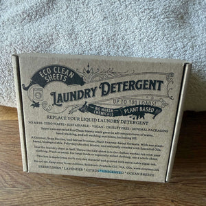 A square kraft paper box of Eco Clean Sheets Laundry Detergent, featuring a detailed product description on the front, set on a wooden surface against a gray textured background.