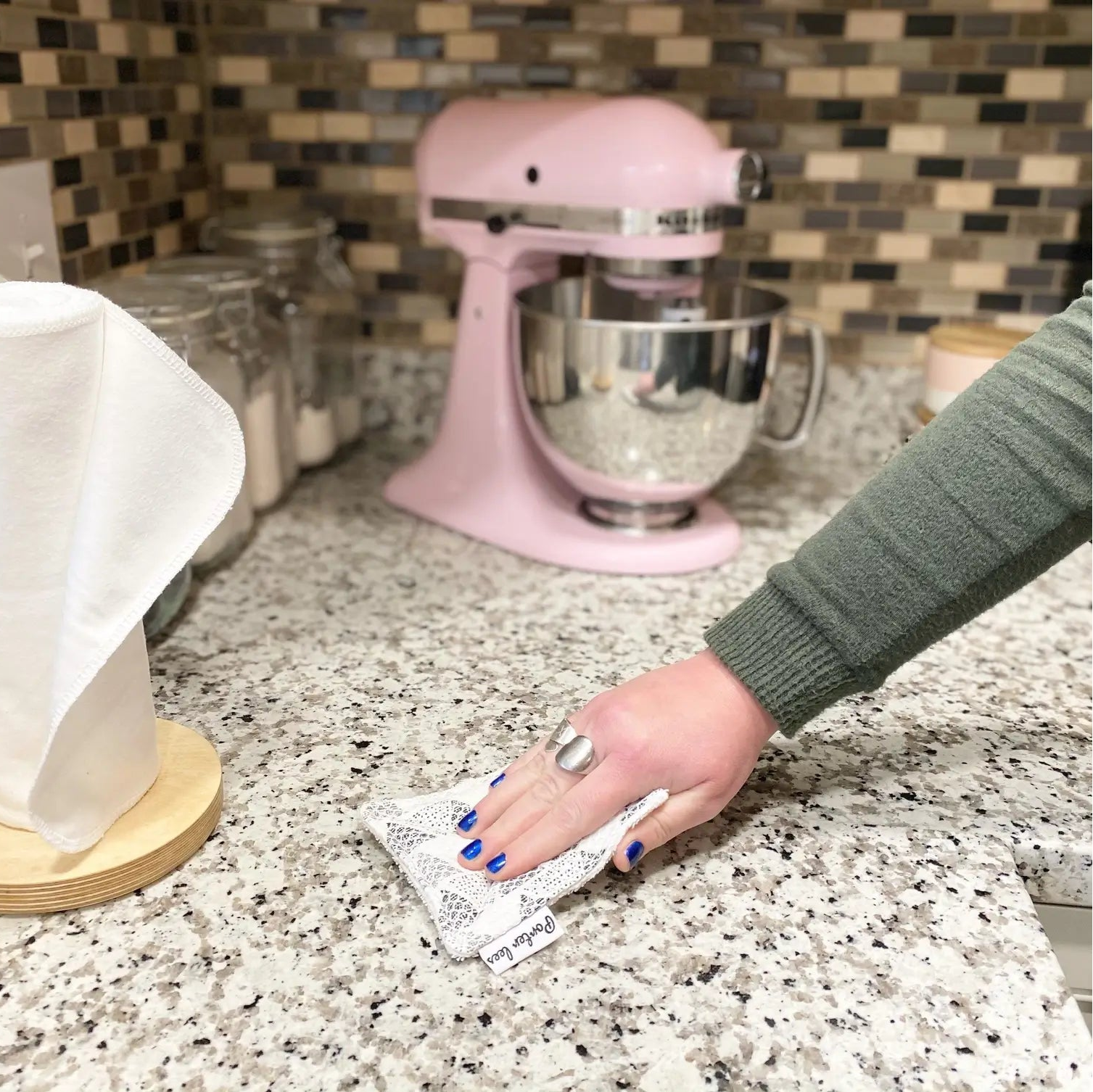 Person cleaning a kitchen counter with a paper towel, pink stand mixer in the background