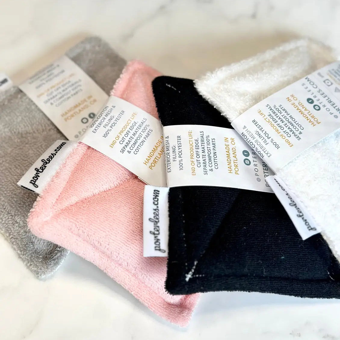 Set of folded towels in gray, pink, and black with labels on a light background