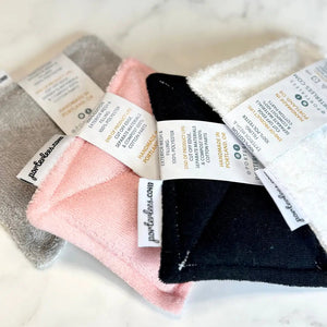 Set of folded towels in gray, pink, and black with labels on a light background