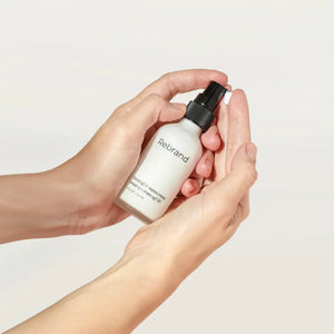 Person holding a small white bottle labeled 'Rebrand' against a plain background
