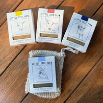 Four packages of Little Seed Farm goat milk soap and an agave exfoliating soap bag on a wooden surface