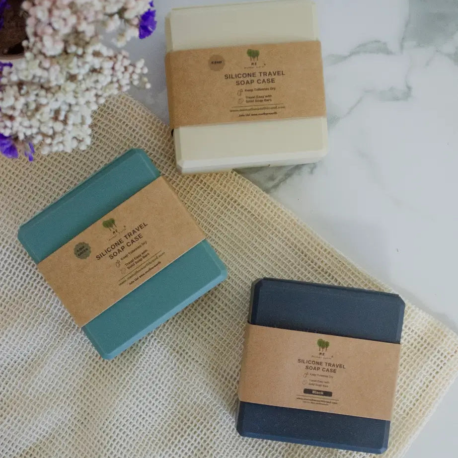 Three silicone travel soap bar cases in brown paper packaging on a textured surface with flowers.
