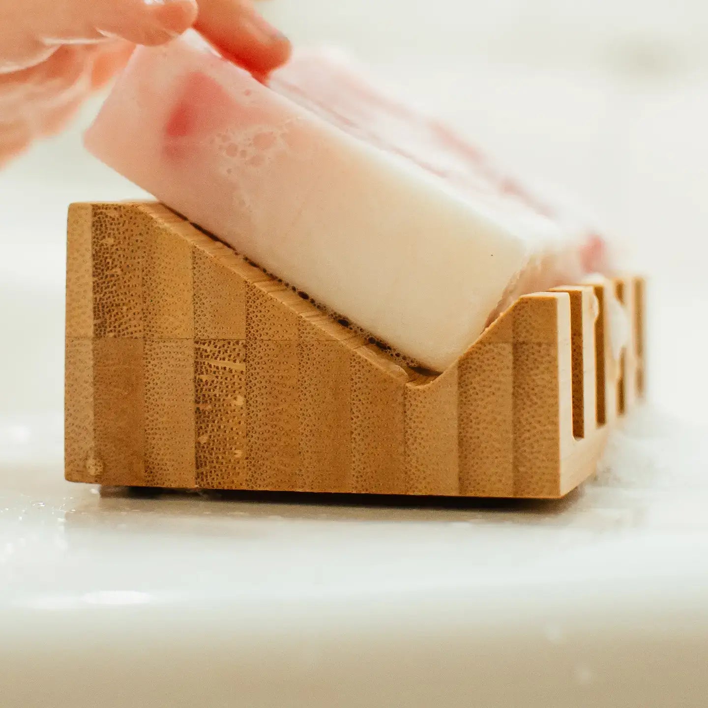 Bar of soap being held above a wooden soap dish on a white background