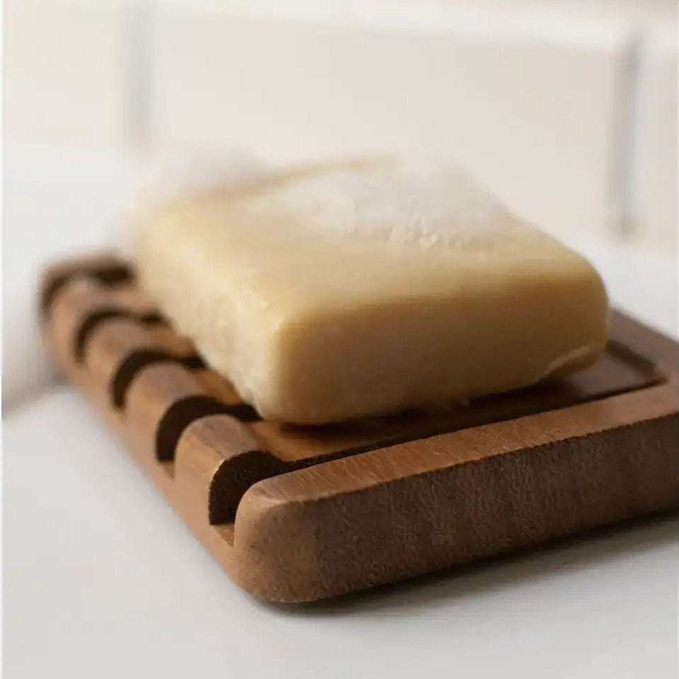 Bar of soap on a wooden soap dish with a neutral background
