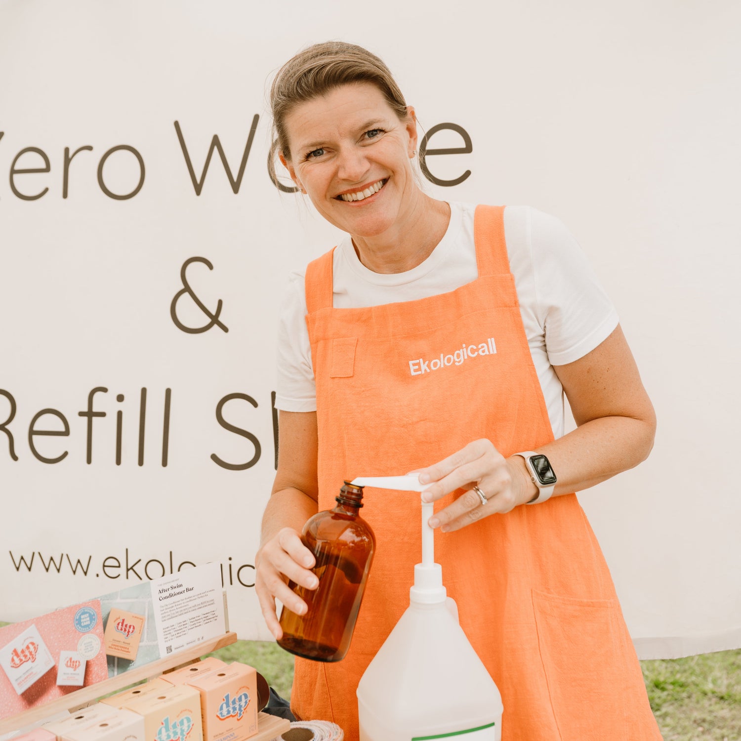 Owner in a coral apron holding a bottle and container at a zero waste refill station.