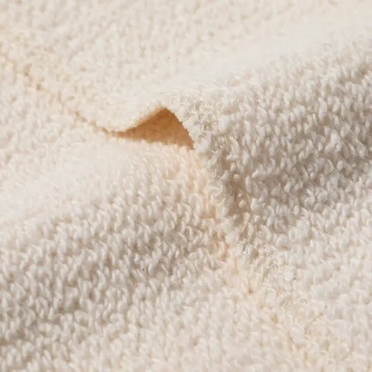 A close-up of a soft, textured cream-colored terry cotton fabric, showing the detailed loop pile and a folded corner.