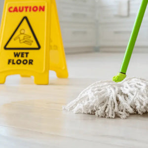 Mop on a wet floor with a yellow 'Caution Wet Floor' sign in the background.