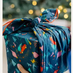 Gift wrapped in a dark blue organic cotton fabric with colorful patterns against a blurred festive background.
