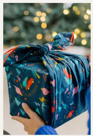 Gift wrapped in a dark blue organic cotton fabric with colorful patterns against a blurred festive background.