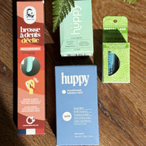 Four dental product packages on a wooden surface with plants in the background