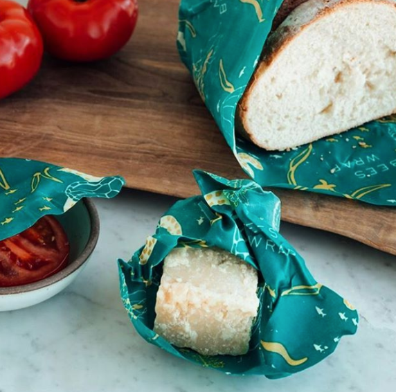 Assorted sizes of Bee's Wrap food storage covers in green color with an ocean pattern, shown wrapping various food items and covering bowls.