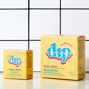 Two yellow packaged shampoo bars with 'DIP' branding and text on them, placed against a tiled wall.