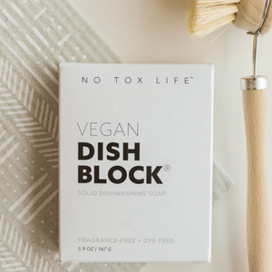 A packaged dish washing block labeled 'VEGAN DISH BLOCK', with a wooden dish brush and a Swedish cloth in the background.