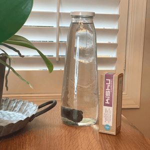 Kishu Charcoal Water Filter in a glass bottle filled with water on a wooden table next to a plant

