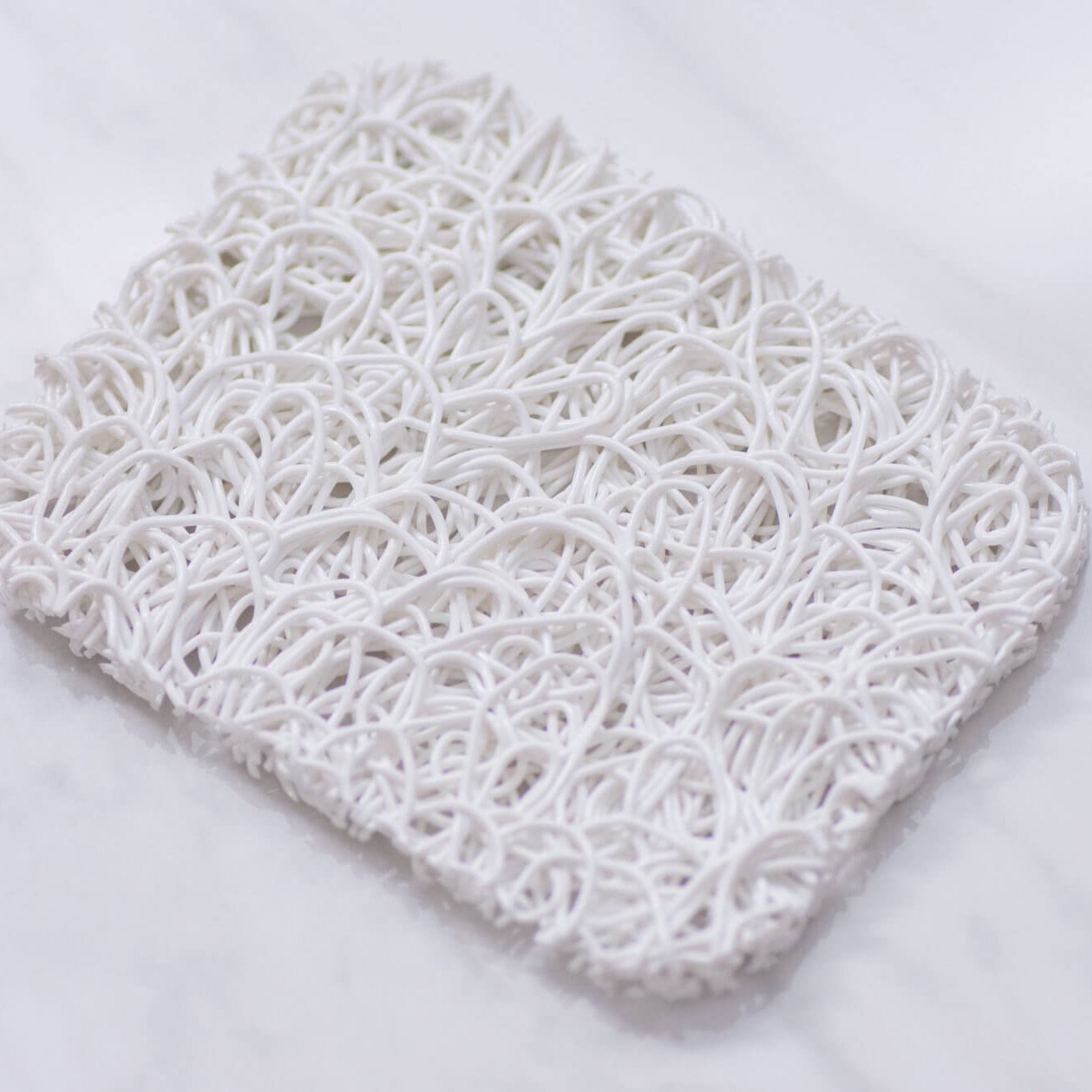 A white, plant-based bioplastic soap lift designed to resemble ramen noodles, placed on a marble surface.