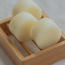 Two solid conditioner bars placed in a wooden soap dish, with a light beige color and a smooth texture visible.