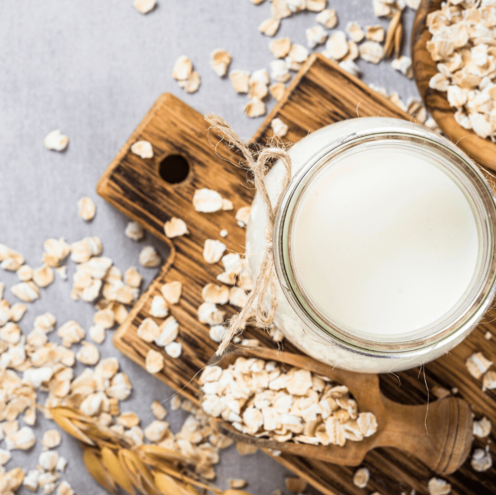 Picture of a glass jar with milk on a wooden tray and oat sprayed around