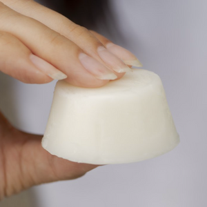 A hand holding a small white deodorant cube.